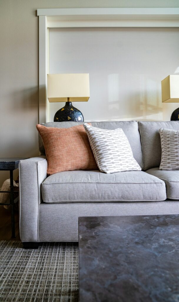 A homeowner measures a neutral sofa in a bright living room beside a coffee table and area rug.